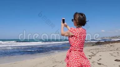 白人妇女拿着相机电话，拍着海上风暴站在海滩上的照片。 她穿着红裙子，戴着<strong>纱丽</strong>